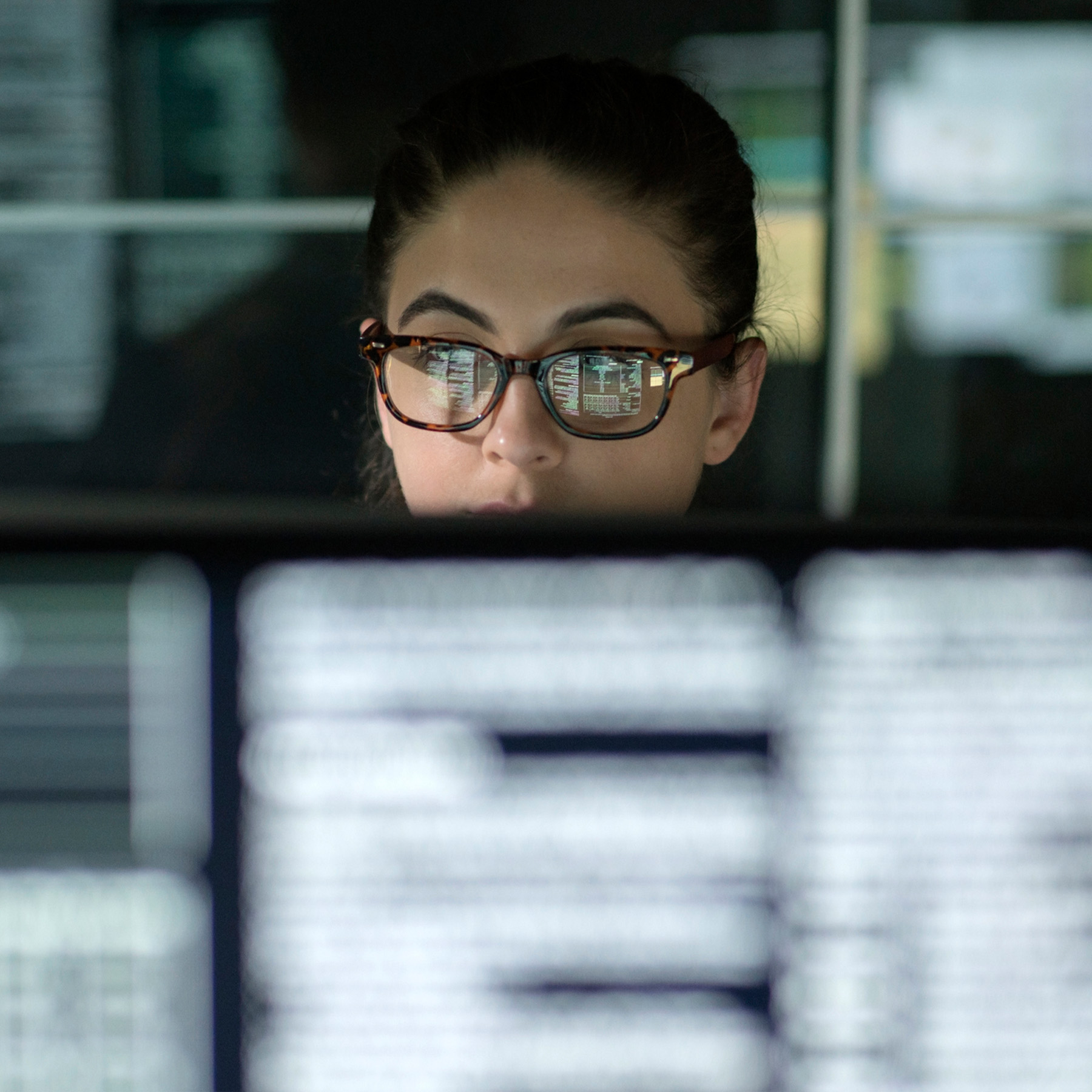 young woman in glasses looking at computer screen blurred in foreground